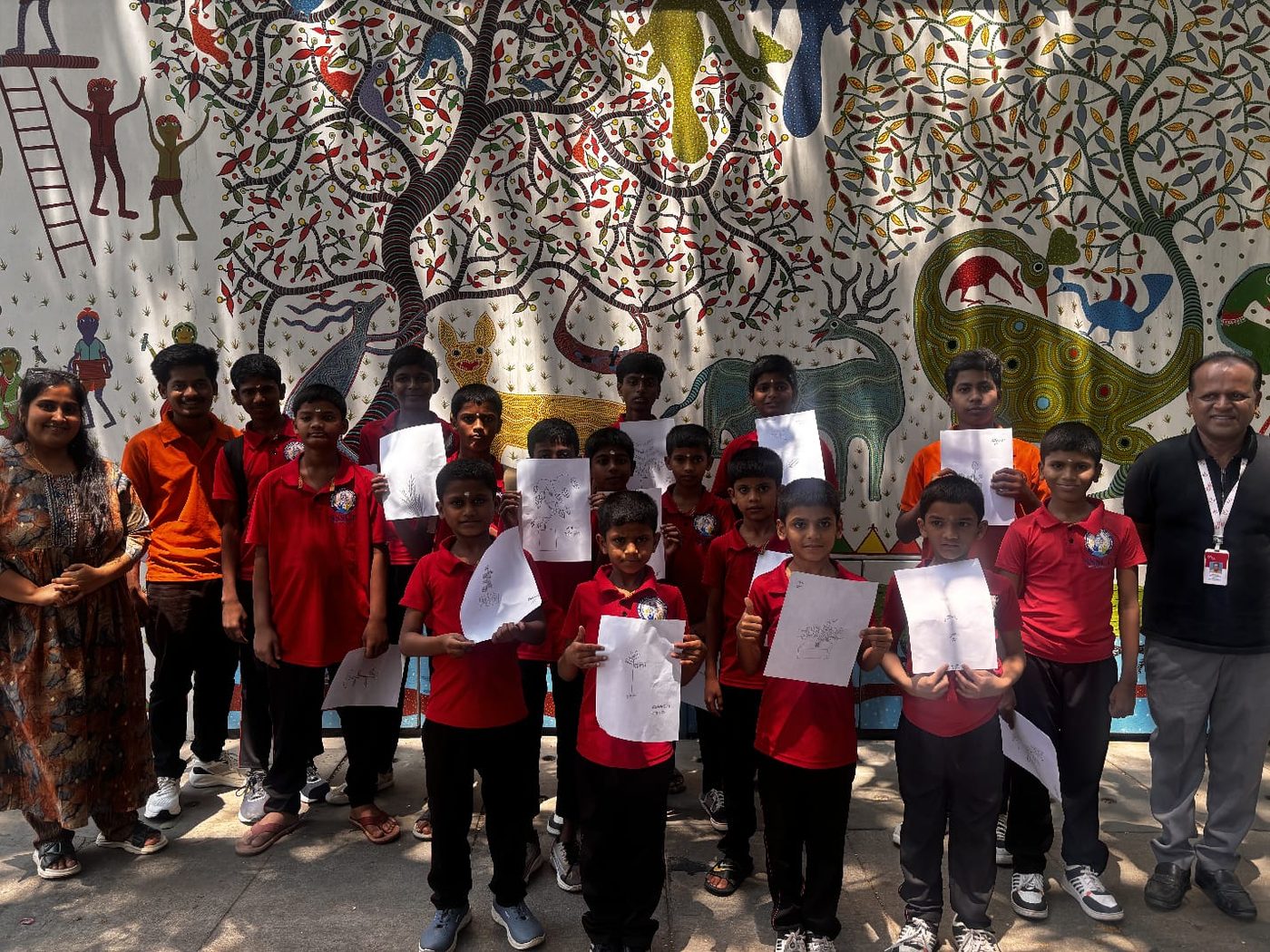 Children showing drawings by a tree-of-life mural